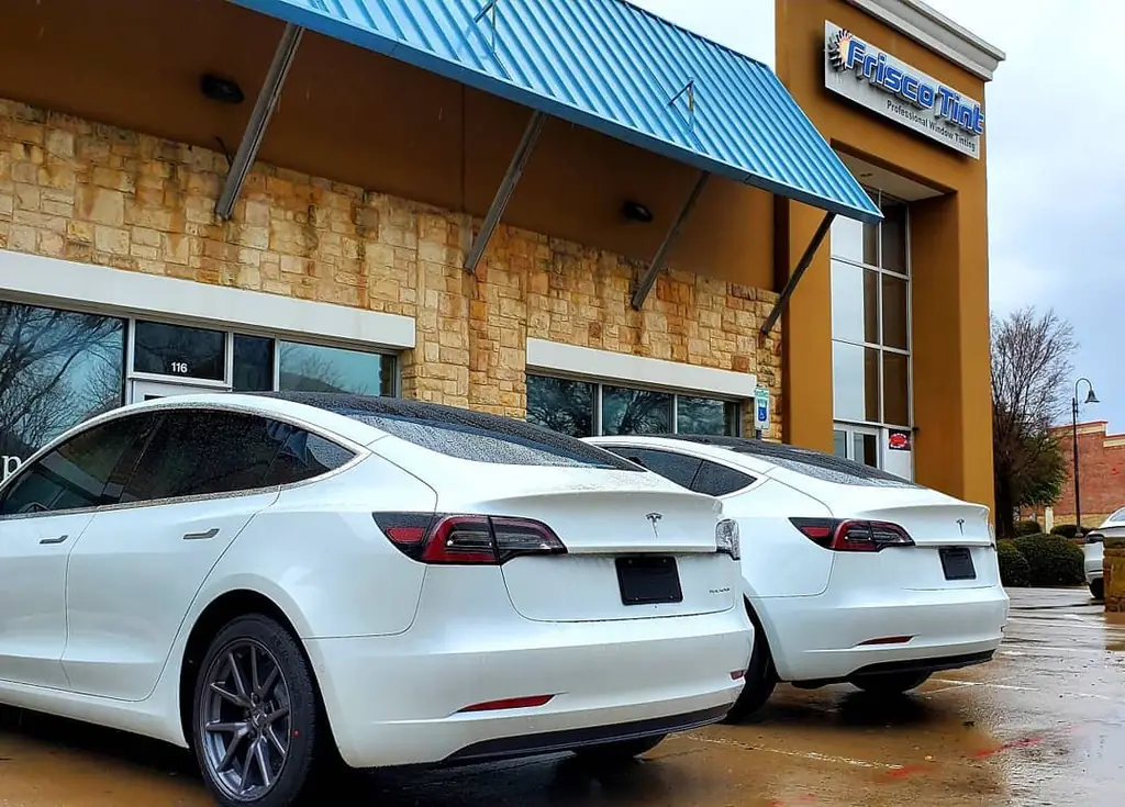 Two tinted white Teslas parked under the Frisco Tint awning